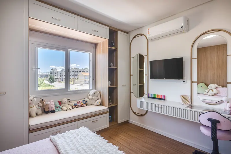 Quarto infantil com banco sob a janela, painel de TV e penteadeira com espelho oval