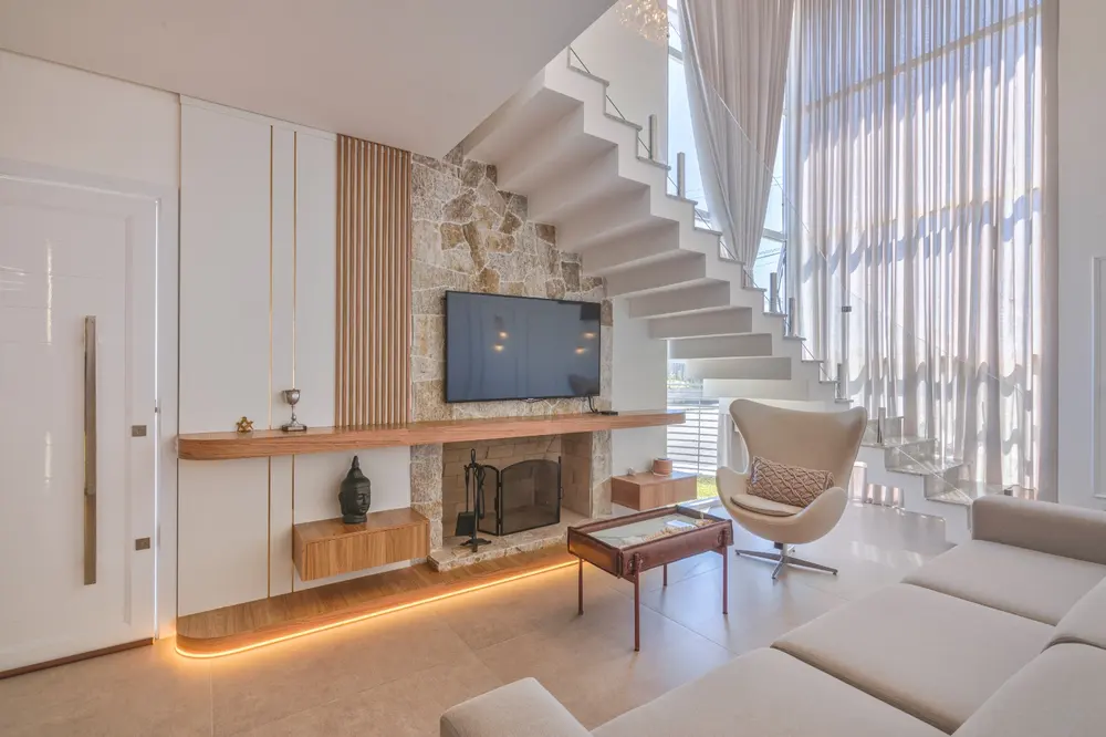 Sala integrada com painel de TV, lareira, prateleiras de madeira e escada