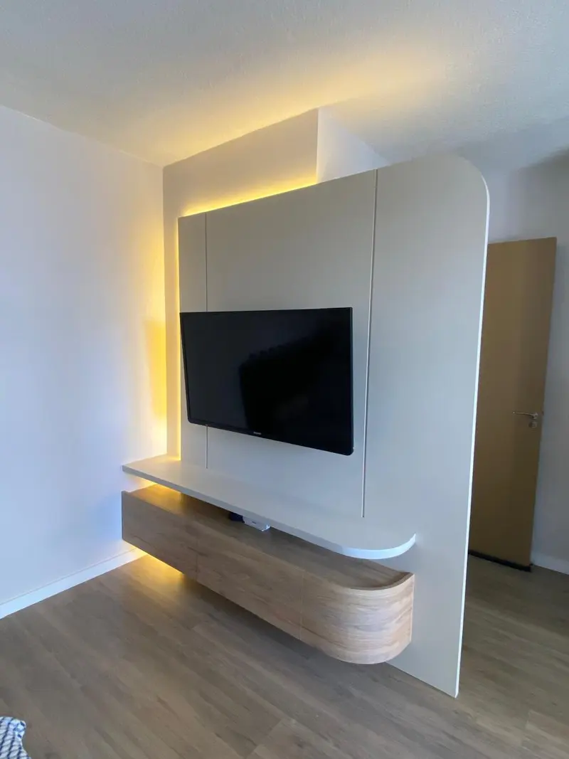 Painel de TV branco com borda arredondada e rack suspenso de madeira